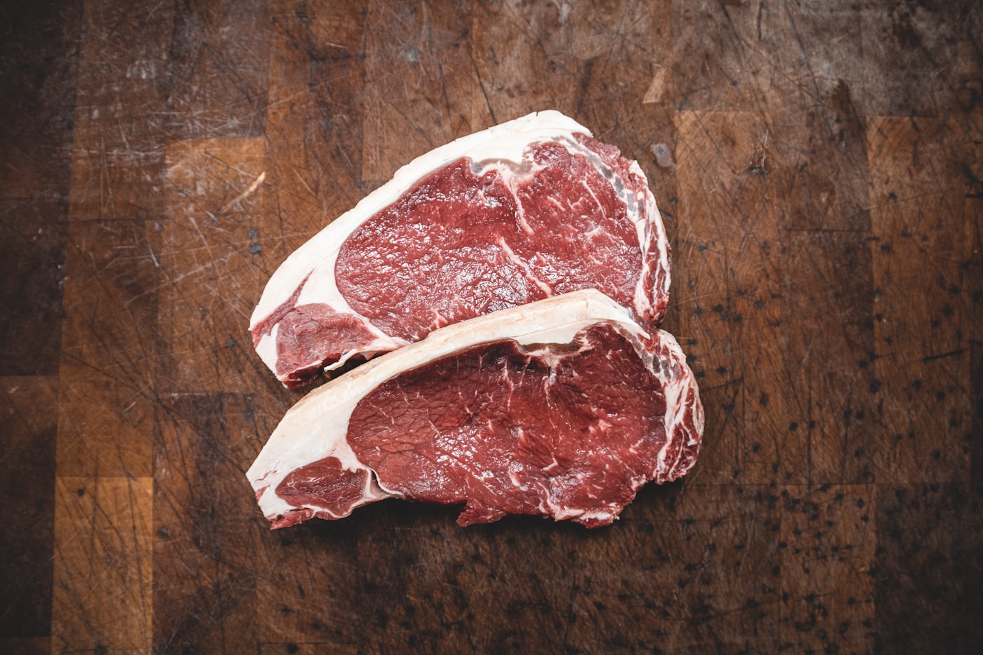 Two heavily marbled raw steaks on a dark wooden board